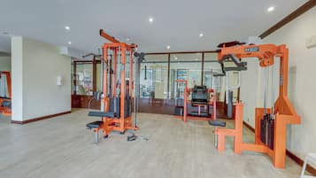 A gym with various exercise machines, a mirror, and a white stool.