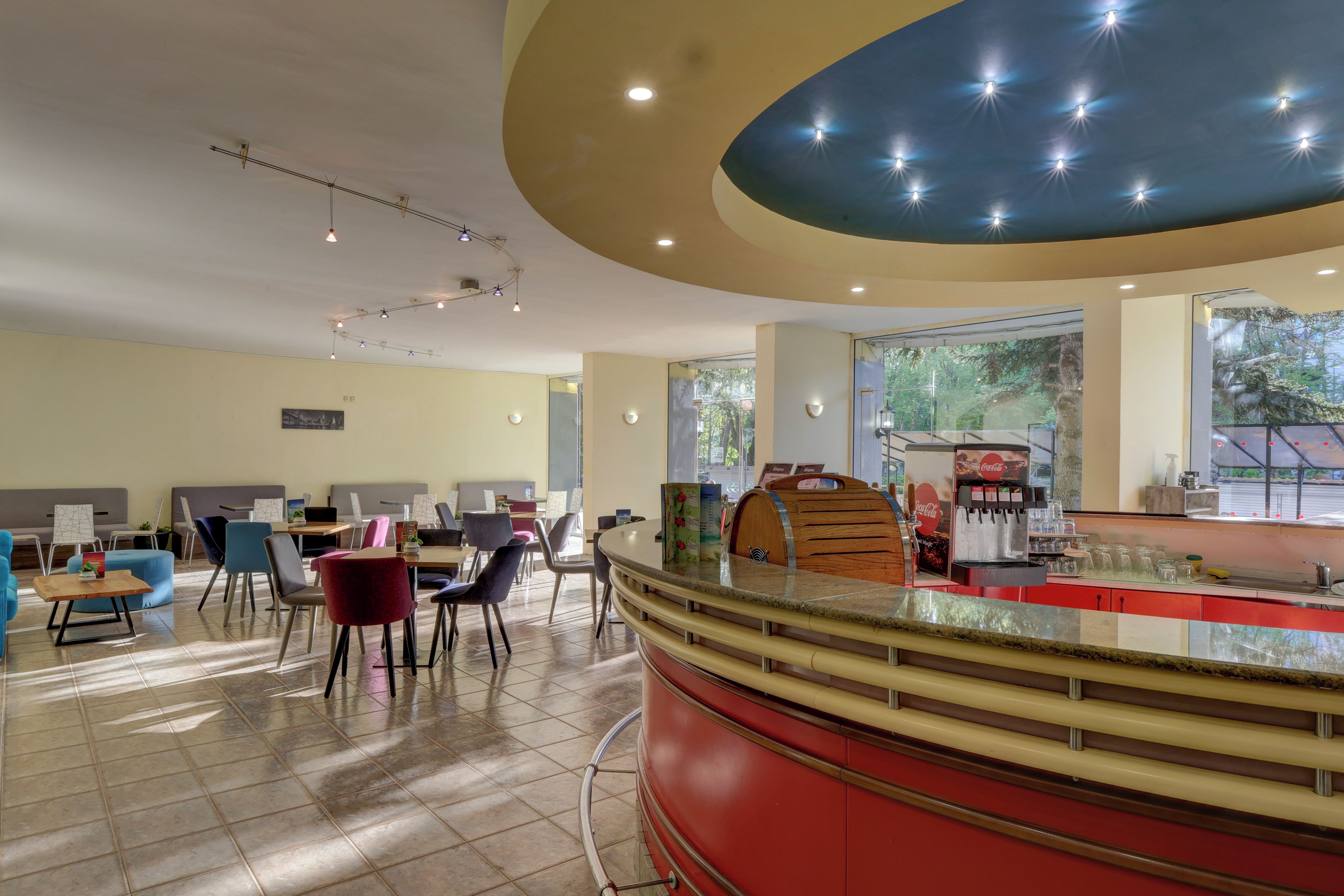 A restaurant with a curved counter, seating area with tables and chairs, and large windows offering a view of the outdoors.