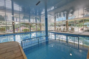 En inomhuspool med väggar av genomskinligt glas, ett kaklat golv och utsikt mot omgivningen.