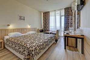 Una habitación de hotel con cama, escritorio, silla, una mesita y ventana con cortinas.