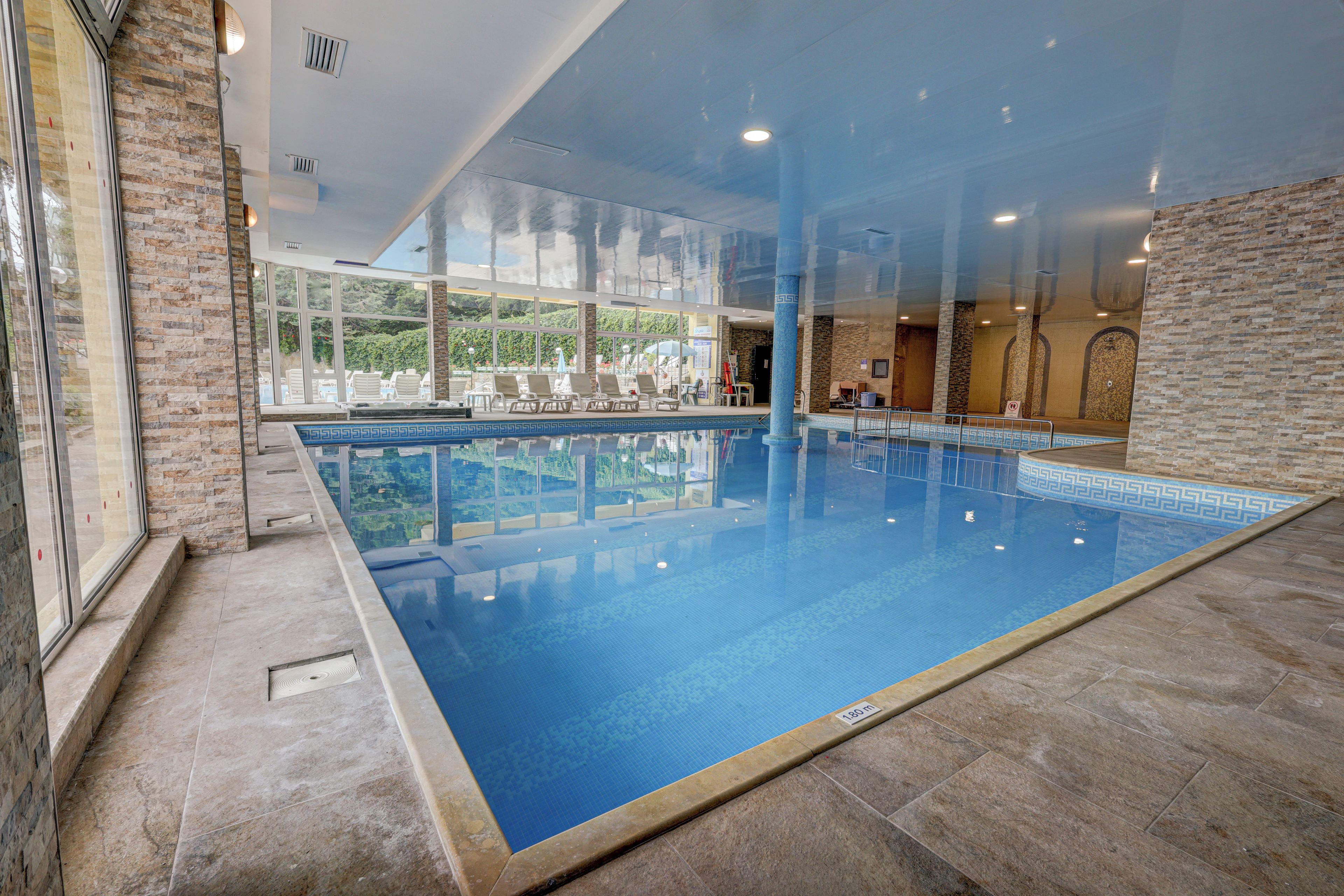 An indoor swimming pool with clear glass walls, a tiled floor, and a view of the outdoors.