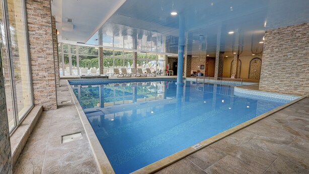 Una piscina interior con paredes de vidrio transparente, suelo de baldosas y vistas al exterior.