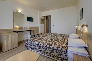 Una habitación de hotel con cama, mesita de noche, espejo y televisor.