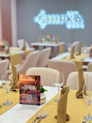 A restaurant setting with tables set for dining, a menu stand, and a neon sign in the background. - Hotel Shipka All Inclusive (Varna)