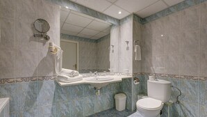 Un baño con lavamanos, espejo, inodoro y un cubo de basura.