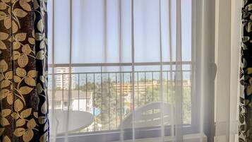A balcony with a view of buildings and trees, a white chair, and a table.