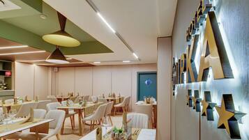 A modern hotel dining area with multiple tables, chairs, and a wall with decorative elements.