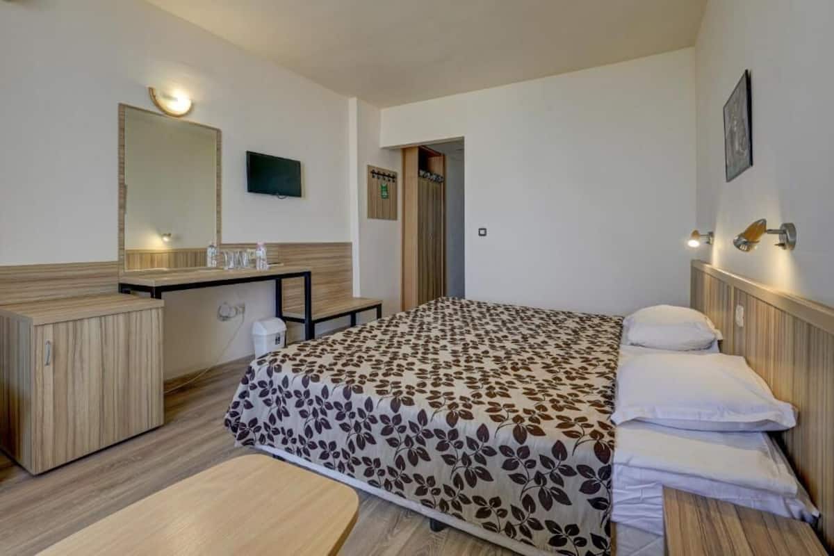 A hotel room with a bed, bedside table, mirror, and a television.