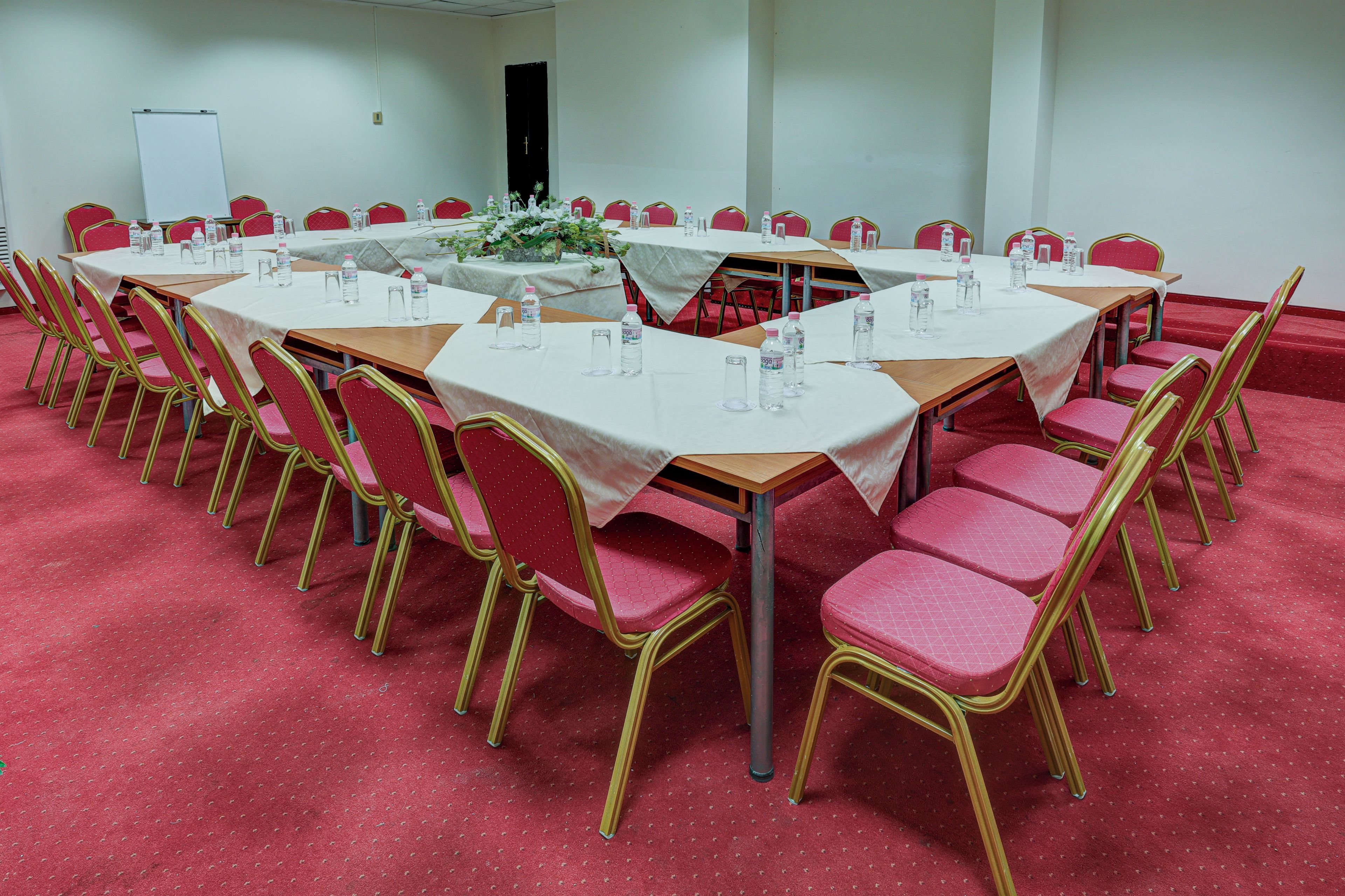 A conference room with multiple tables and chairs, white tablecloths, and water bottles.