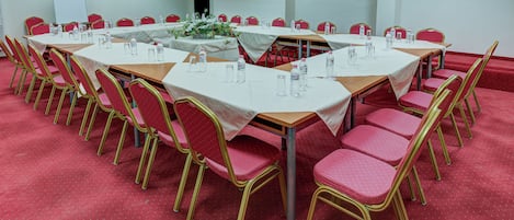 A conference room with multiple tables and chairs, white tablecloths, and water bottles.
