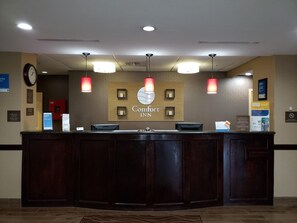 A reception desk with a sign reading 'Comfort Inn,' overhead lighting, a clock, and a 'Check In/Check Out' sign. - Comfort Inn (Marion)