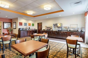 Un comedor de hotel con mesas y sillas, una zona de cocina con electrodomésticos y un suelo estampado.