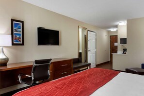 Ein Hotelzimmer mit Bett, Schreibtisch, Stuhl, Fernseher und einer Tür zu einem weiteren Raum.