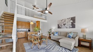Ein geräumiger Wohnbereich mit Esstisch, Sofa, Treppe und Deckenventilator.