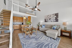 A spacious living area with a dining table, a sofa, a staircase, and a ceiling fan.
