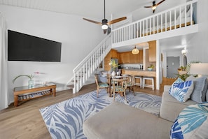 A spacious living area with a high ceiling, a staircase leading to an upper level, a dining area, and a kitchen.