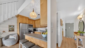 Eine moderne Küche mit Holzschränken, einem Edelstahlkühlschrank, einer zentralen Kochinsel mit Sitzgelegenheiten und einer Pendelleuchte.
