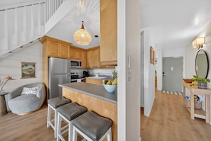 A modern kitchen with wooden cabinets, a stainless steel refrigerator, a central island with stools, and a hanging light fixture.