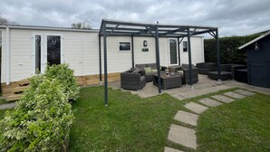 Ein Mobilheim mit einer Terrassenfläche, die Gartenmöbel und eine Pergola beinhaltet.