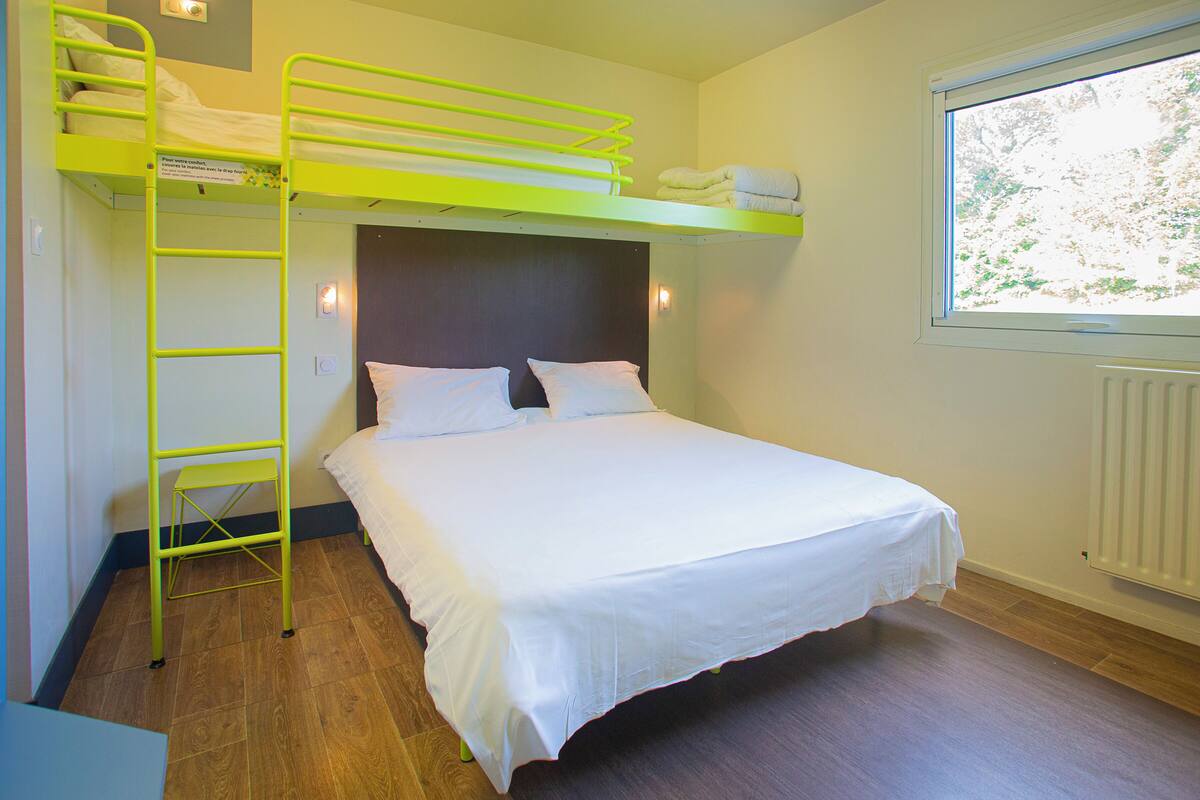 Uma cama beliche com escada, uma cama de solteiro, roupa de cama branca, uma janela com vista e um radiador.