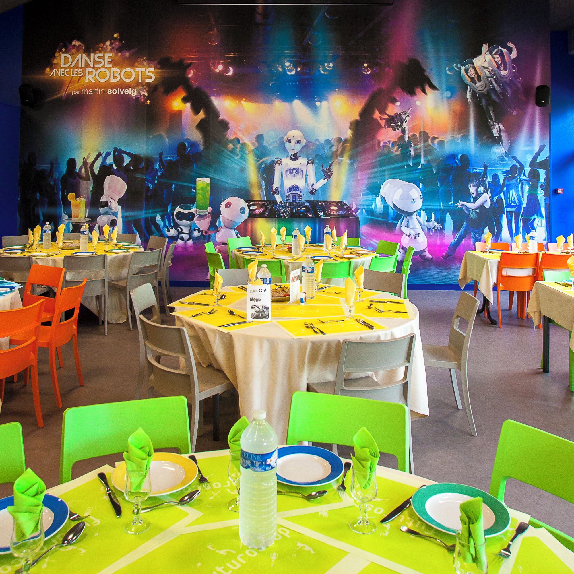 A restaurant with round tables, green and orange chairs, and a colorful robot-themed backdrop.