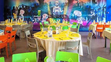 A restaurant with round tables, green and orange chairs, and a colorful robot-themed backdrop.