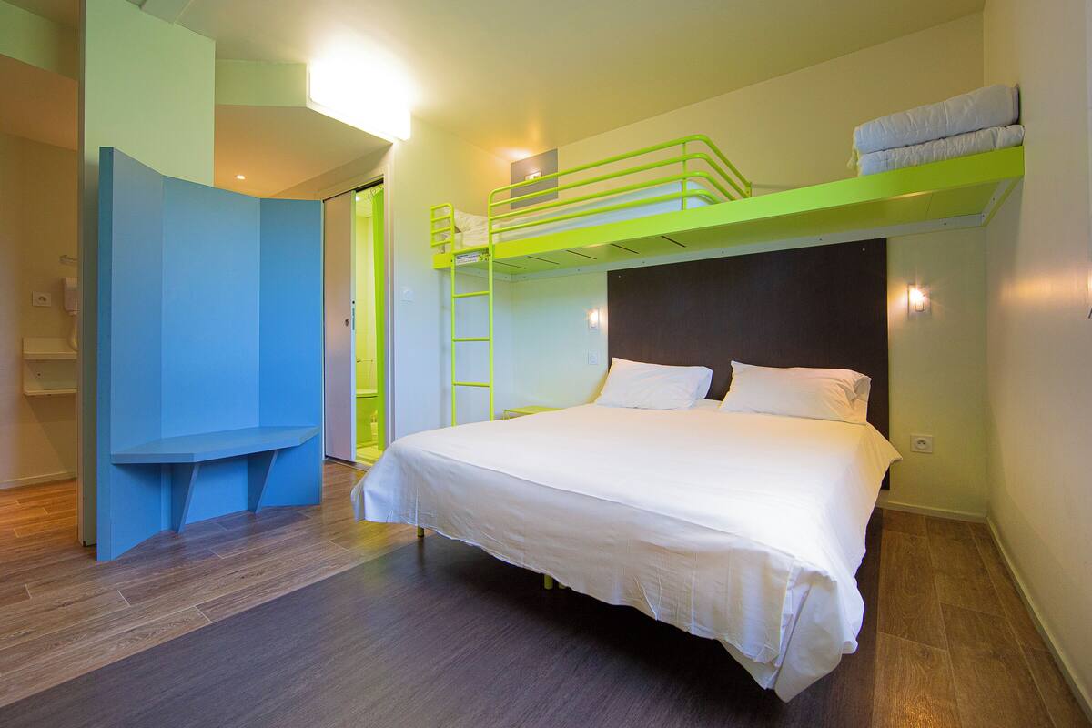 Uma cama beliche com escada, uma colcha branca e um banco azul.