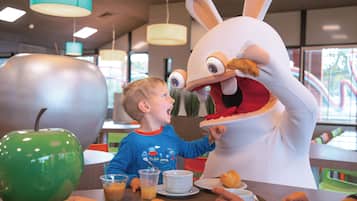 A dining area with a large green apple, a white rabbit mascot, and a child interacting with the mascot.