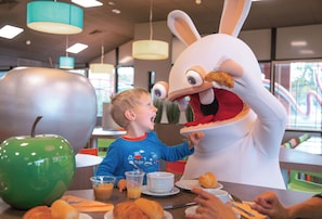 A dining area with a large green apple, a white rabbit mascot, and a child interacting with the mascot. - Hotel du Futuroscope (Chasseneuil-du-Poitou)