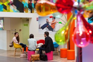 A modern interior with colorful seating, a large poster, and a visible fire exit sign. - Hotel du Futuroscope (Chasseneuil-du-Poitou)