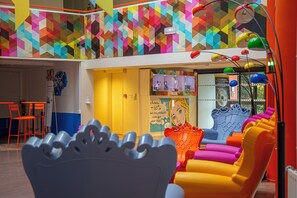 A colorful interior with a geometric-patterned wall, a blue sofa, and a yellow and orange chair. - Hotel du Futuroscope (Chasseneuil-du-Poitou)