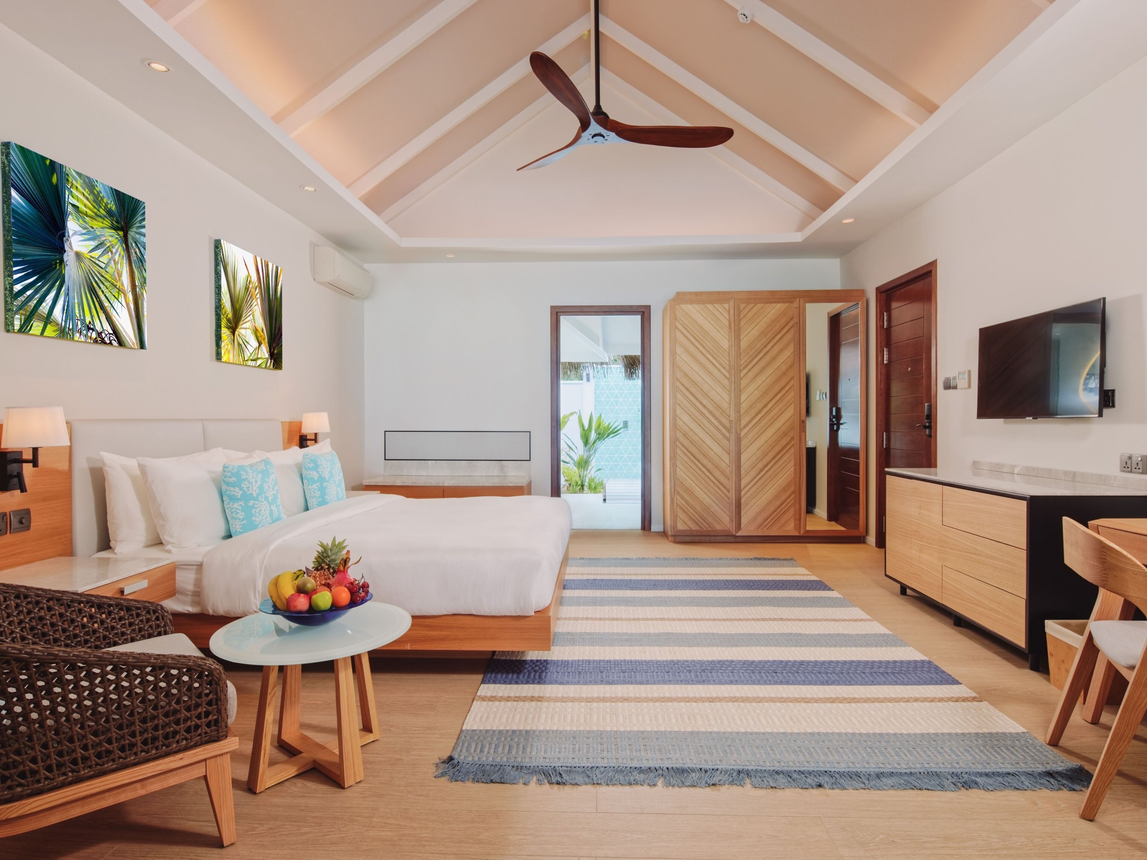 A modern hotel room with a bed, bedside table, TV, wardrobe, and a view of the outdoors.