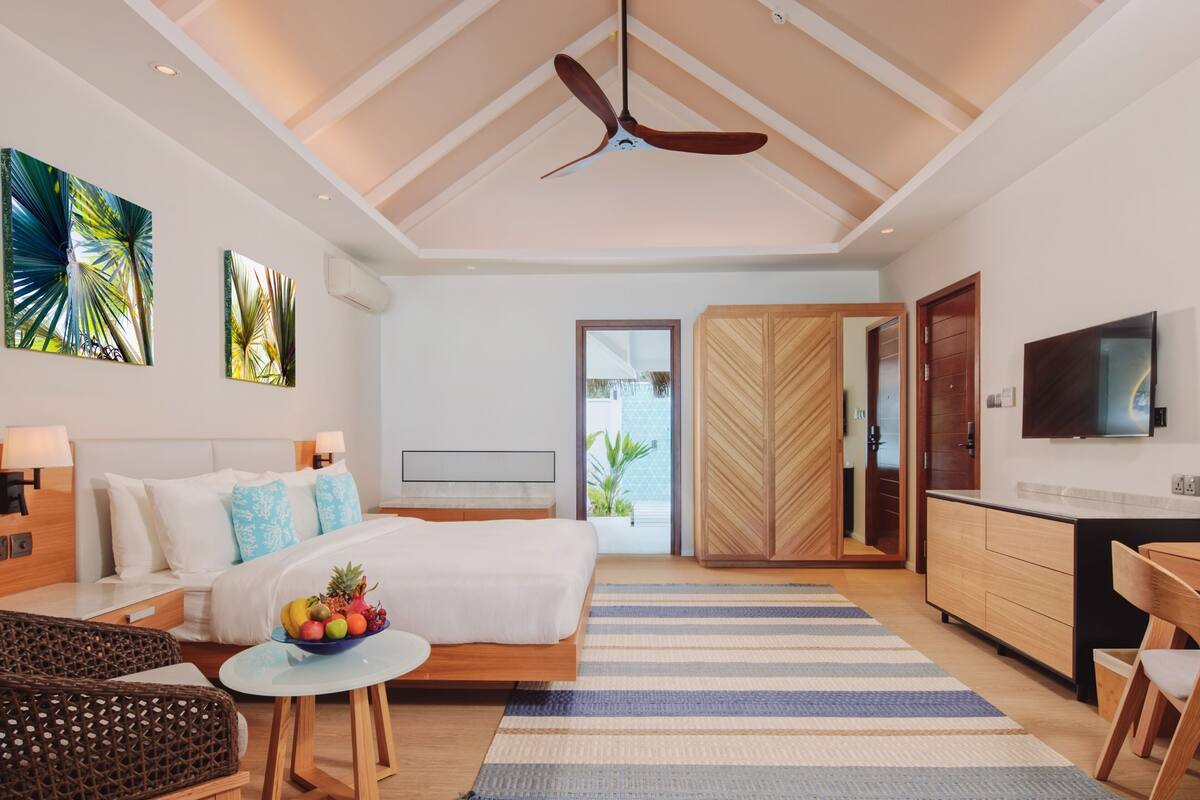 A modern hotel room with a bed, bedside table, TV, wardrobe, and a view of the outdoors.