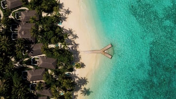 An aerial view of a beach resort with overwater bungalows, clear turquoise waters, and palm trees.