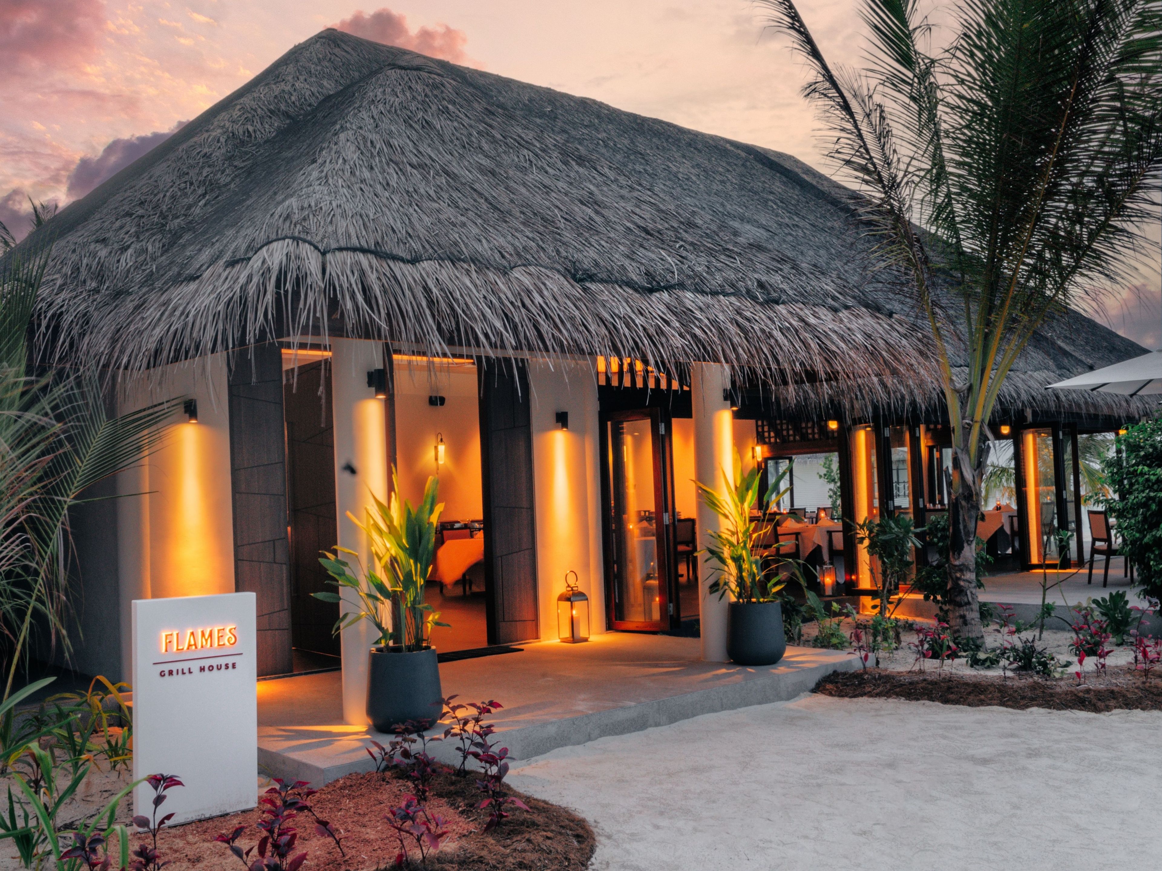 A thatched-roof building with a sign reading 'Flames Grill House.'