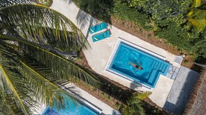 An aerial view of a swimming pool with a person swimming, surrounded by palm trees and a sandy area. - Nova Maldives (Malé)