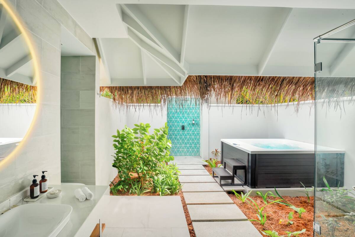 A modern bathroom with a bathtub, a shower, a glass-enclosed hot tub, and a small garden area with plants.