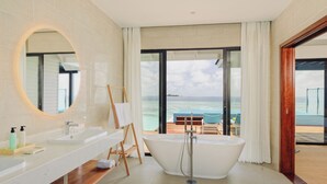 A modern bathroom with a freestanding bathtub, a large mirror, and a view of the ocean through a glass door. - Nova Maldives (Malé)