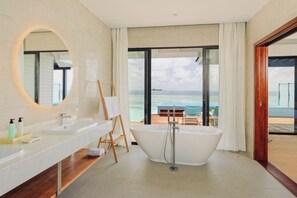 A modern bathroom with a freestanding bathtub, a large mirror, and a view of the ocean through a glass door. - Nova Maldives (Malé)