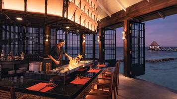 A restaurant with a chef preparing food, a bar area, and a view of the sea.