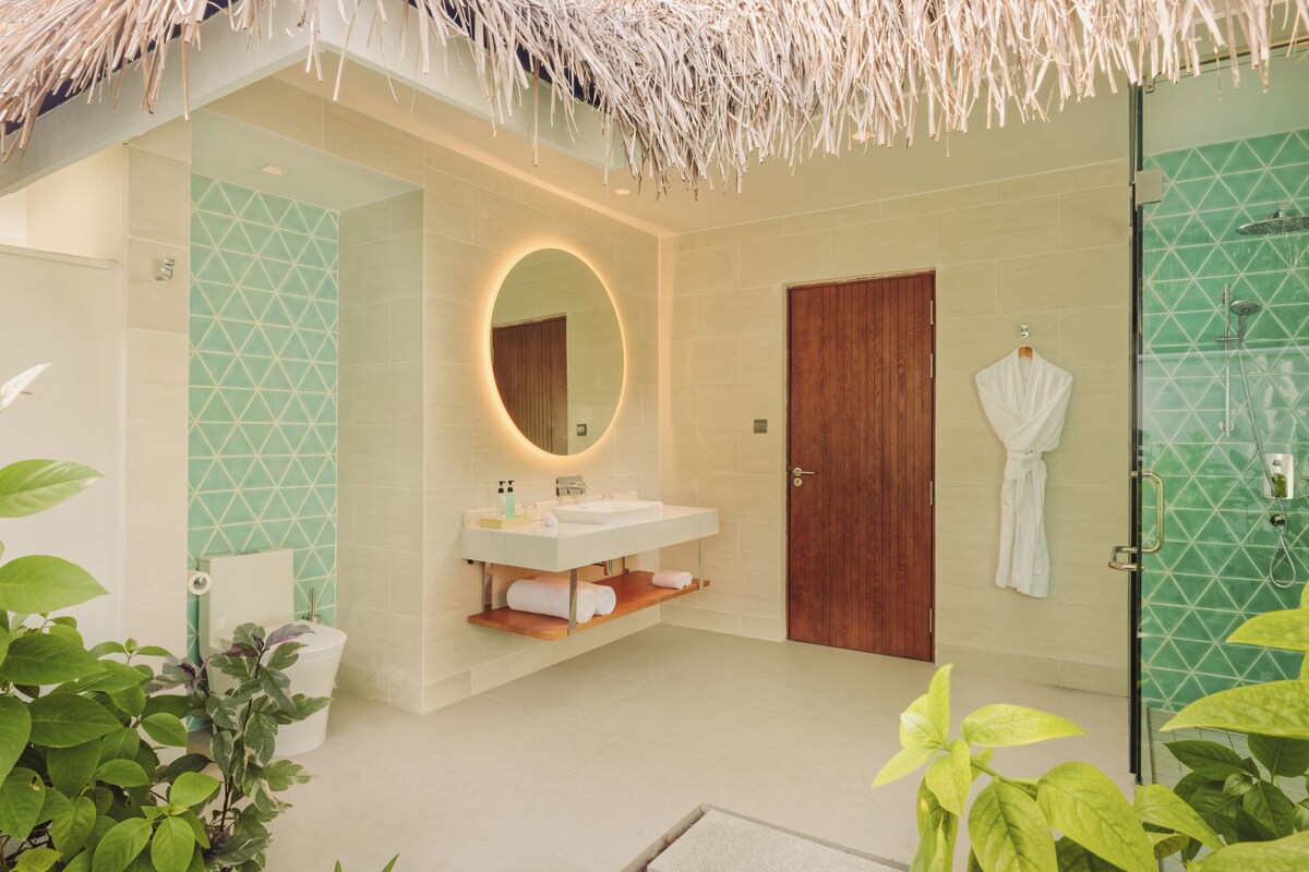 A modern bathroom with a vanity, a round mirror, a wooden door, and a glass shower enclosure.