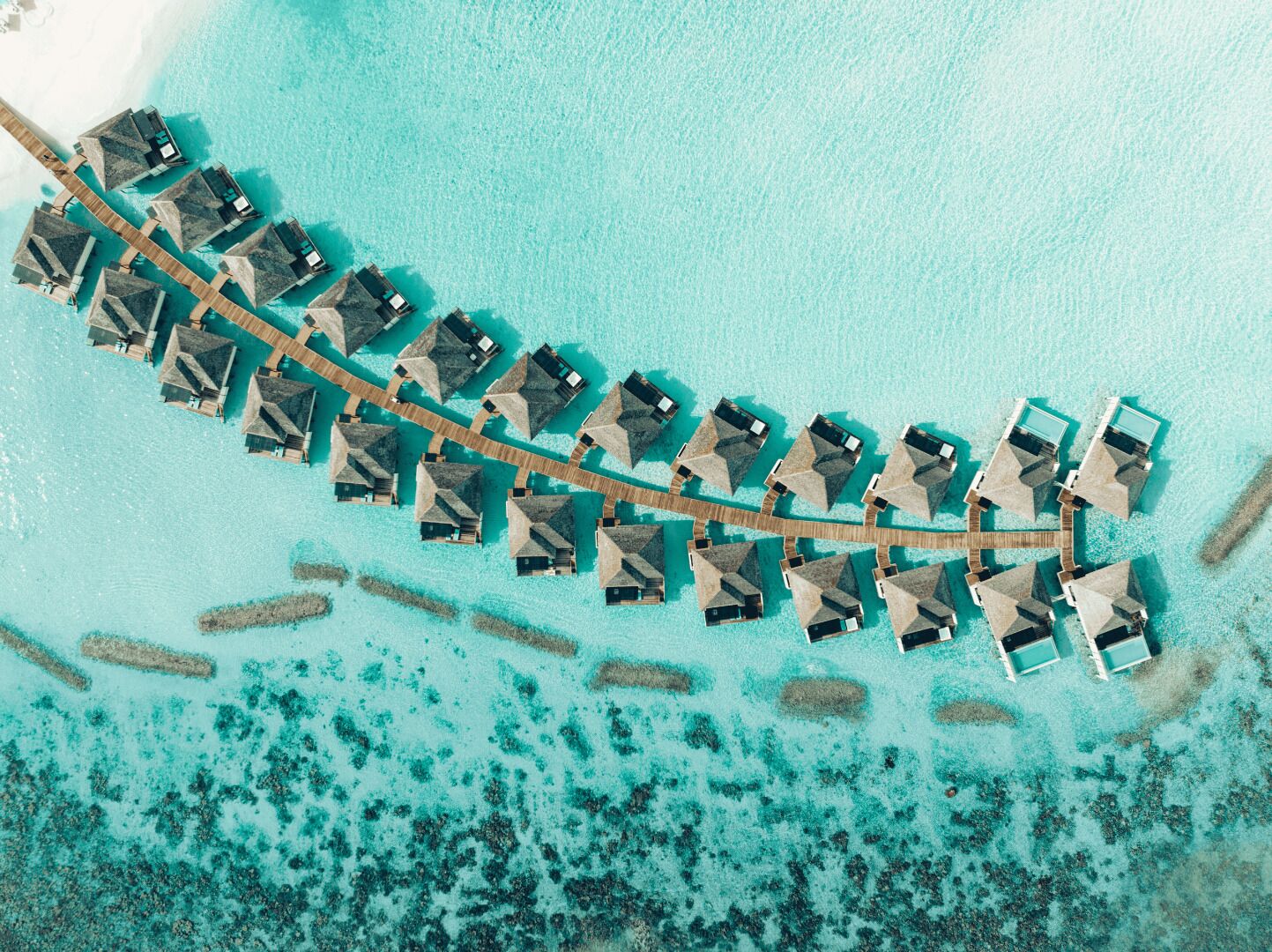 An aerial view of overwater bungalows arranged in a curved formation, connected by wooden walkways.