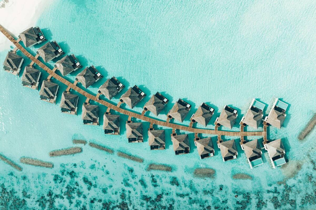 An aerial view of overwater bungalows arranged in a curved formation, connected by wooden walkways.