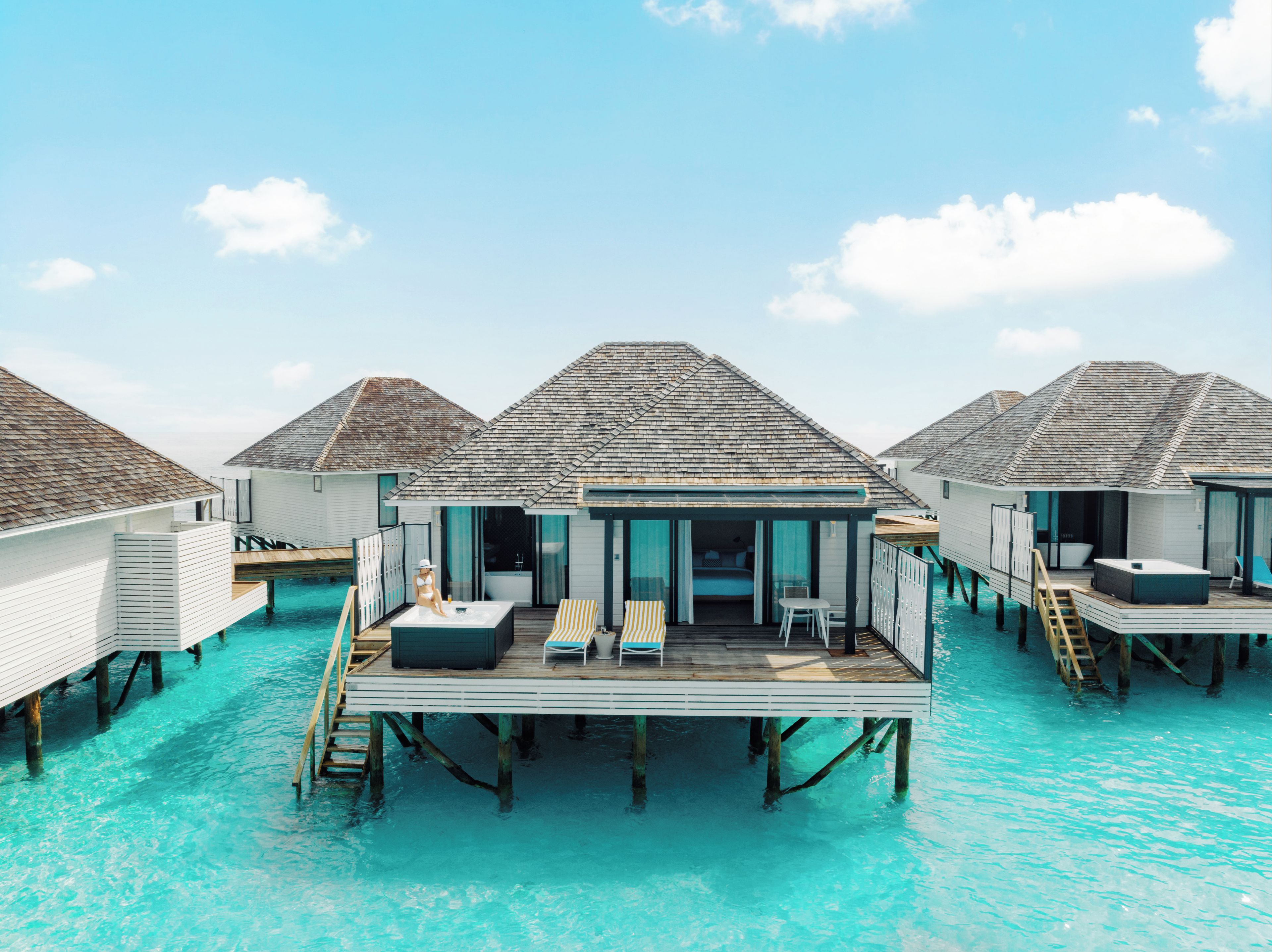 Bungalows sobre el agua con piscinas privadas, terrazas de madera y sillones de descanso.