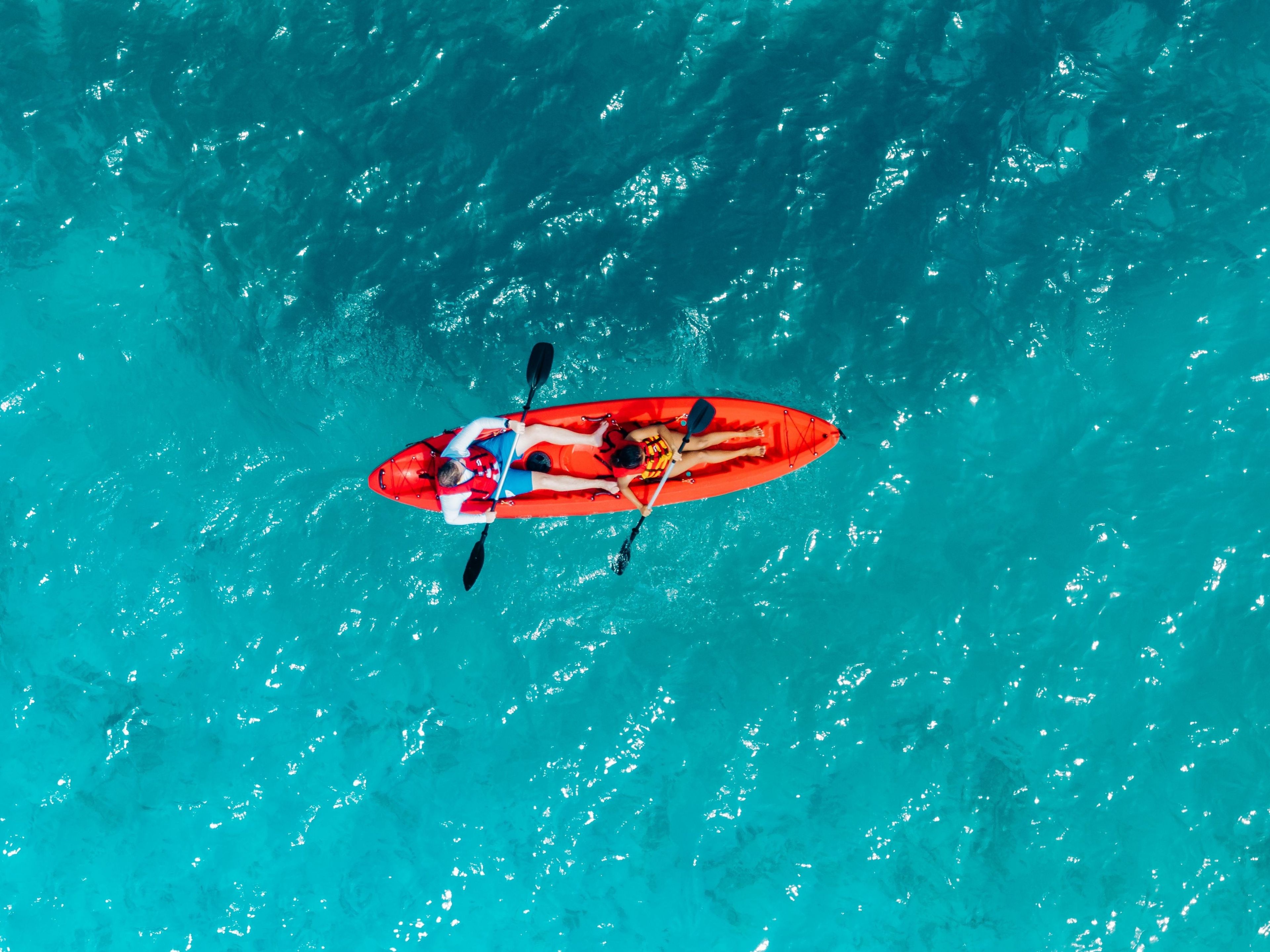 Un kayak rojo con dos personas remando en aguas turquesas.