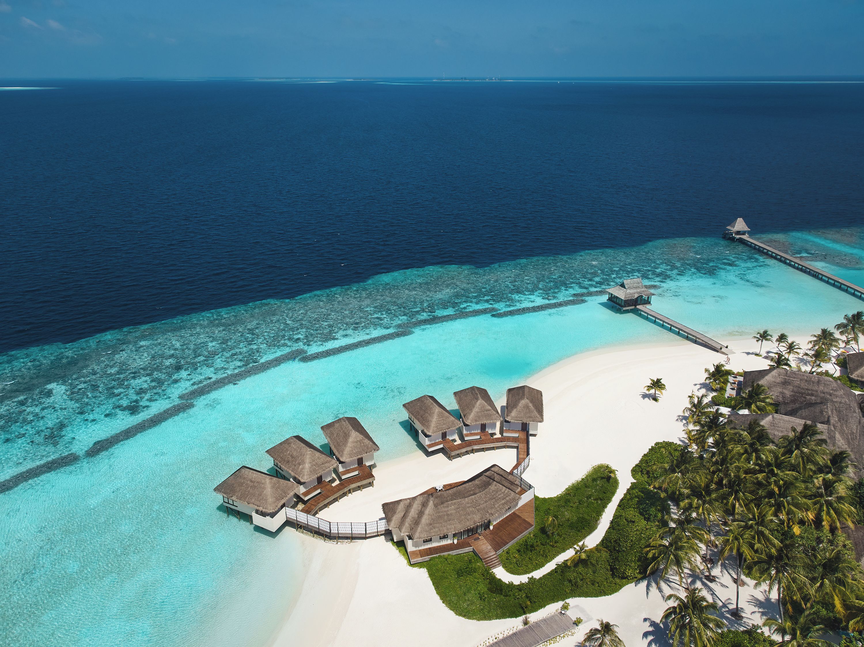 An aerial view of a resort with overwater bungalows, a beach, and a pier.