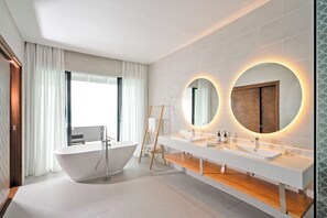 Un baño moderno con una bañera independiente, lavamanos dobles y grandes espejos con iluminación circular.
