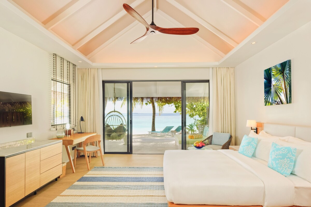 A modern hotel room with a bed, desk, and a view of the ocean.