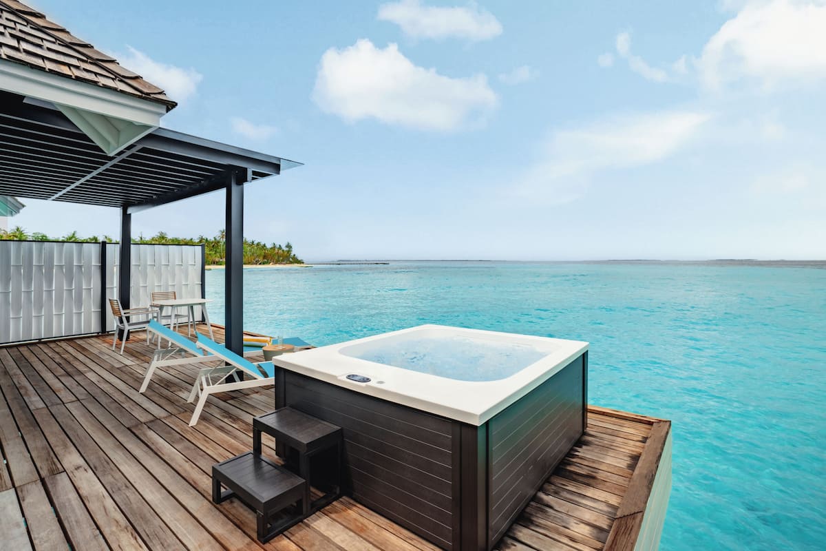 A wooden deck with a hot tub, lounge chairs, and a covered seating area overlooking a clear blue sea.