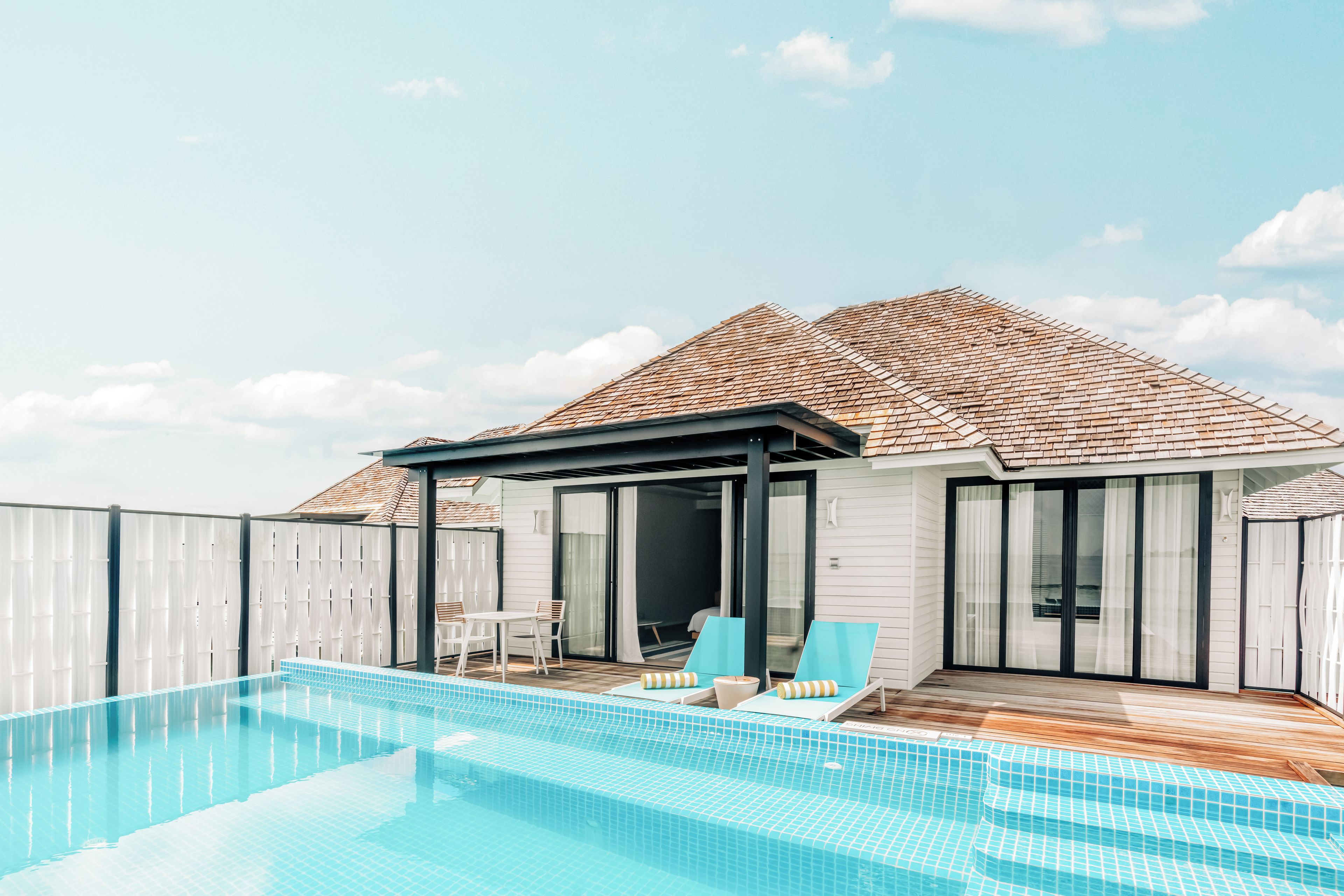 Un área moderna junto a la piscina, con piscina cristalina, sillas de descanso y un porche cubierto.